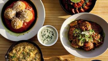 A wooden table with various dishes including a bowl of fried chicken, a skillet with vegetables, and flatbreads.