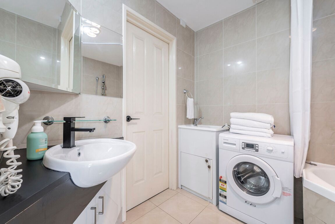A modern bathroom with a white sink, a hairdryer, a washing machine, and a mirror.