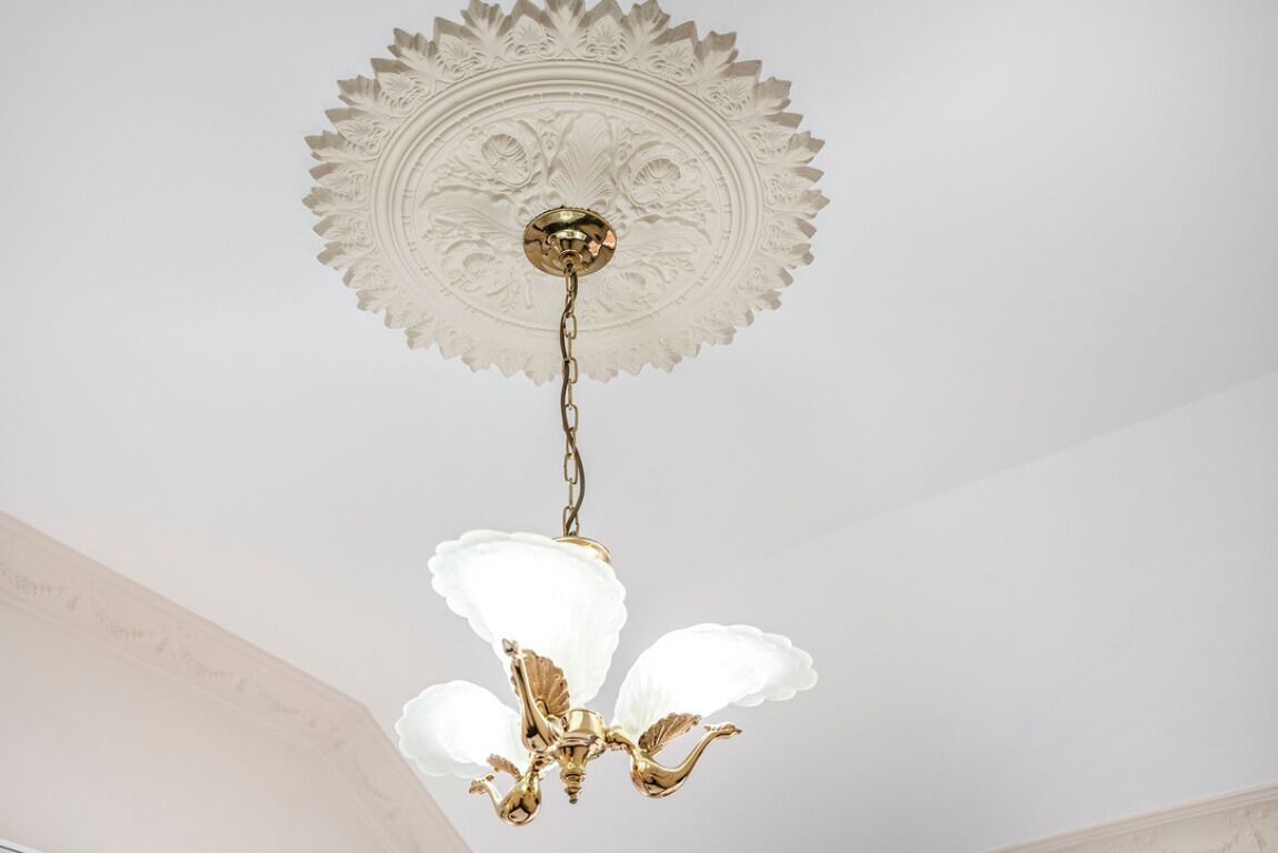 A chandelier with a white, ornate ceiling medallion and a gold chain.