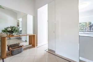 Un interior moderno con una consola de madera, cestas de mimbre, un espejo grande y vistas a un balcón.