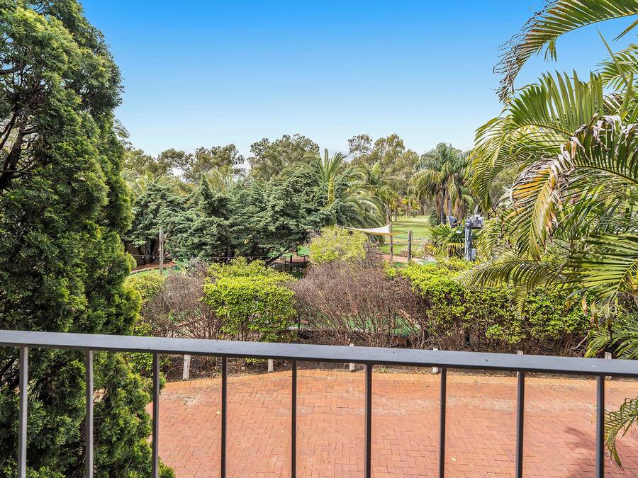 Un jardin aménagé avec un chemin en briques, différents arbres et un ciel bleu dégagé.