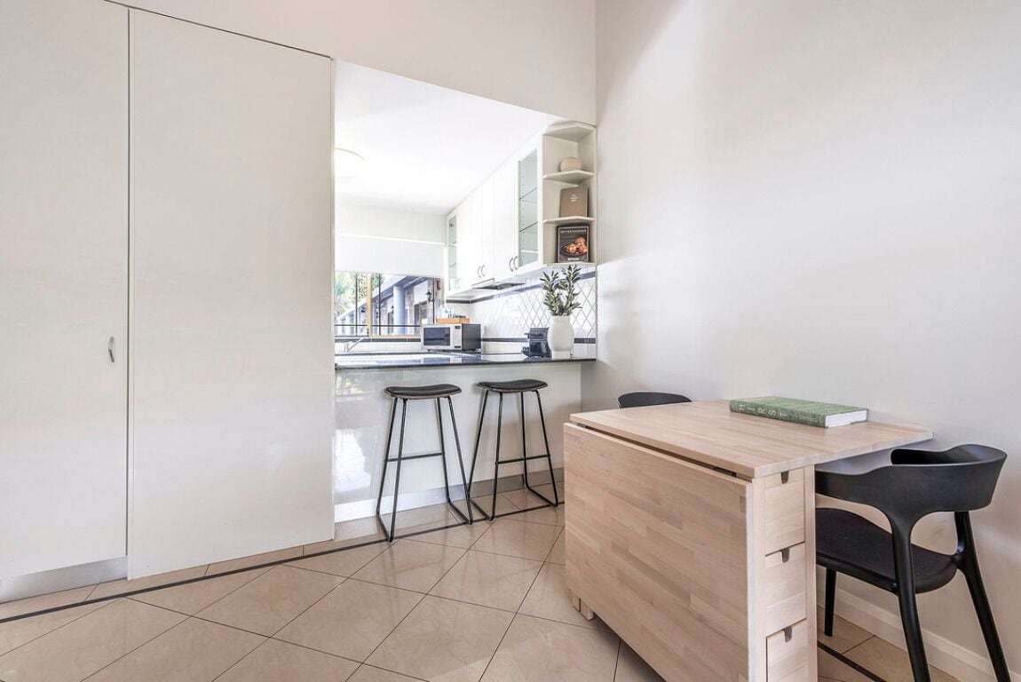 Una cocina moderna con armarios blancos, encimera de madera y dos taburetes.