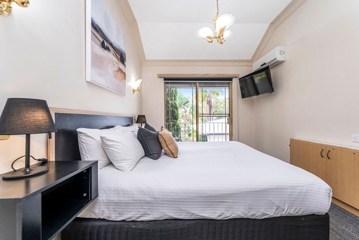 Un dormitorio con cama, mesitas de noche, un televisor instalado en la pared y una ventana con vistas al exterior.