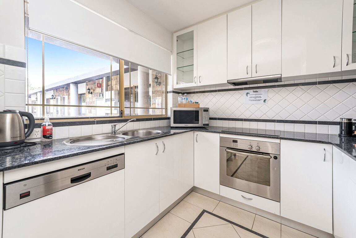 A modern kitchen with white cabinets, a stainless steel oven, a microwave, and a sink.