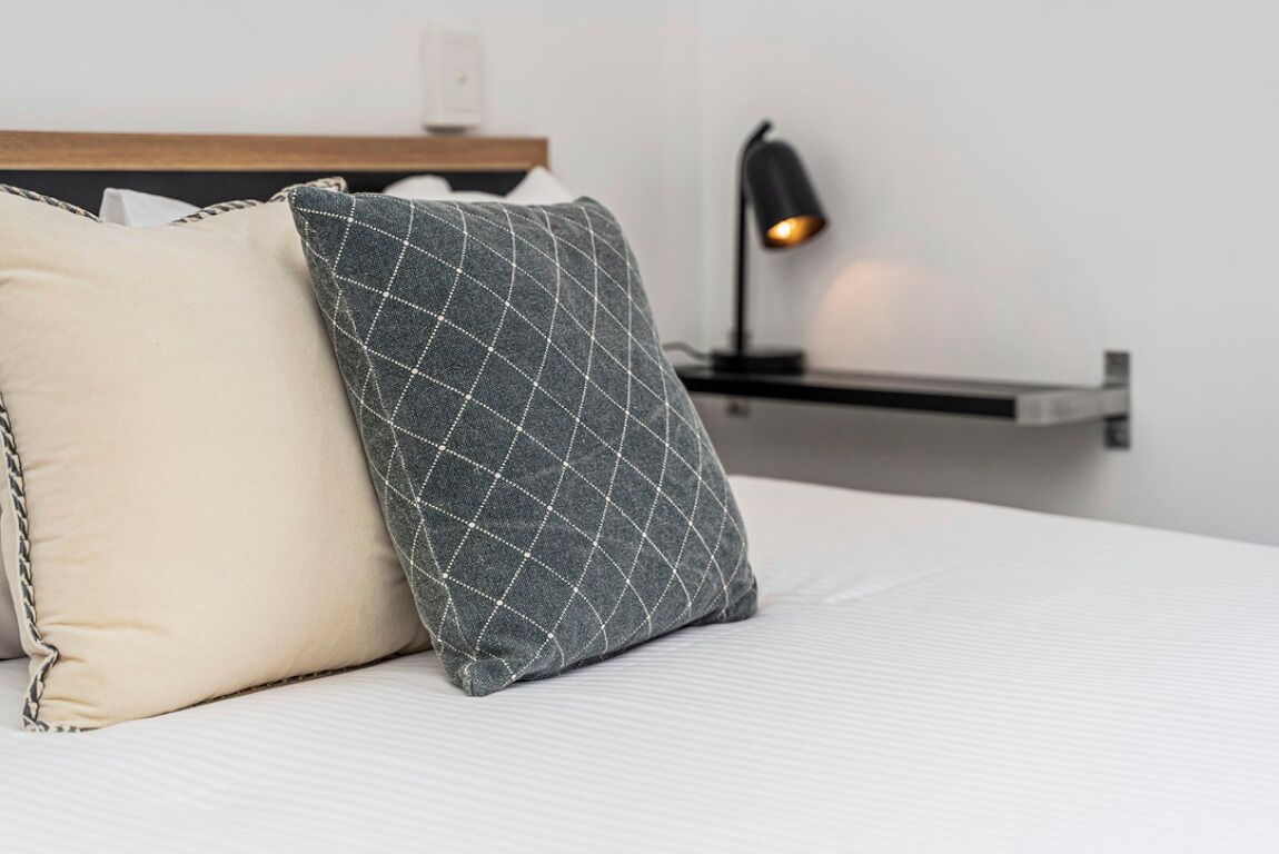Un lit avec deux oreillers, une table de chevet avec une lampe et une étagère fixée au mur.