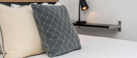 A bed with two pillows, a bedside table with a lamp, and a wall-mounted shelf.