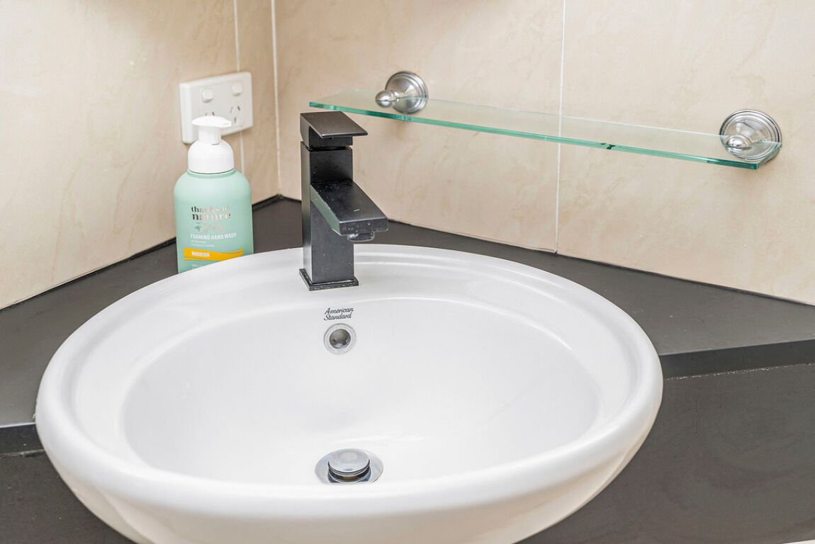 A bathroom with a white sink, a glass shelf, and a bottle of hand soap.