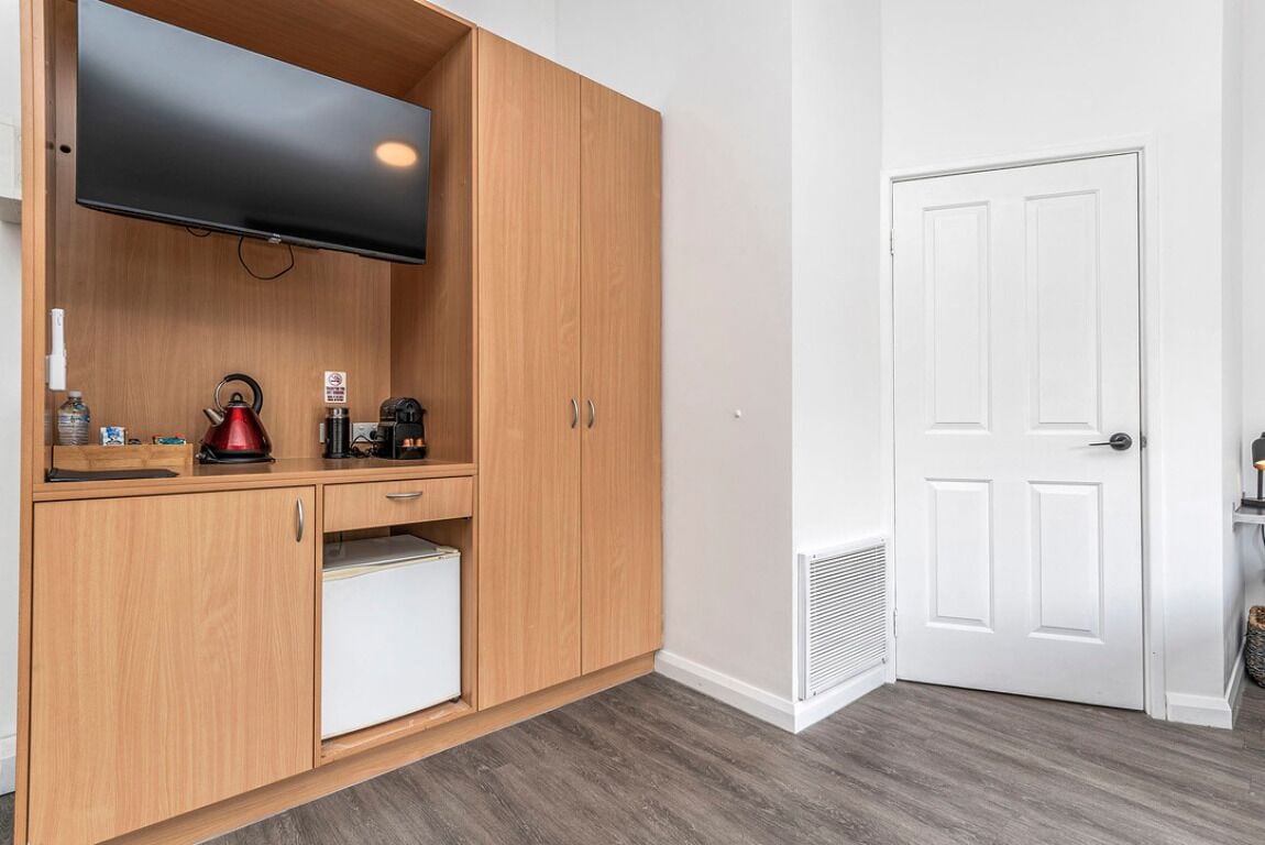 Una cocina compacta con armarios de madera, un refrigerador empotrado y un televisor de pantalla plana montado sobre la encimera.