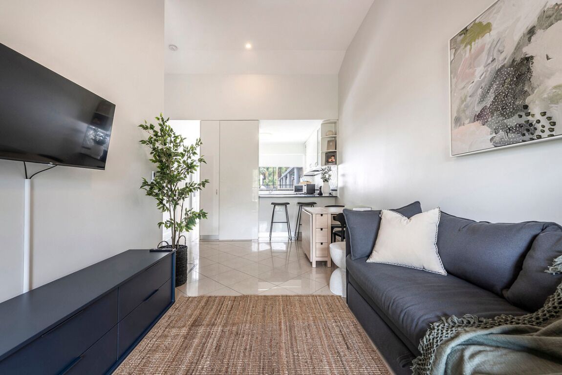 A modern living room with a flat-screen TV, a dark sofa, a coffee table, and a large abstract painting on the wall.