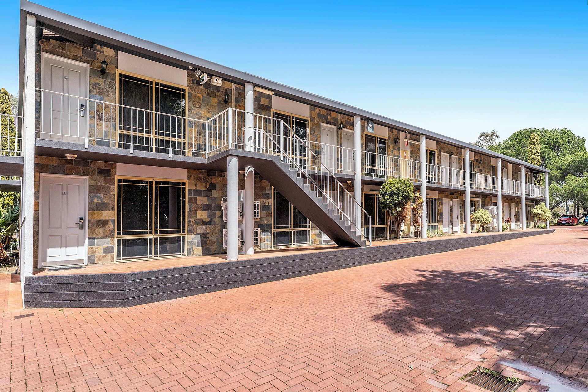 A multi-story hotel with a stone facade, a central staircase, and a covered walkway.