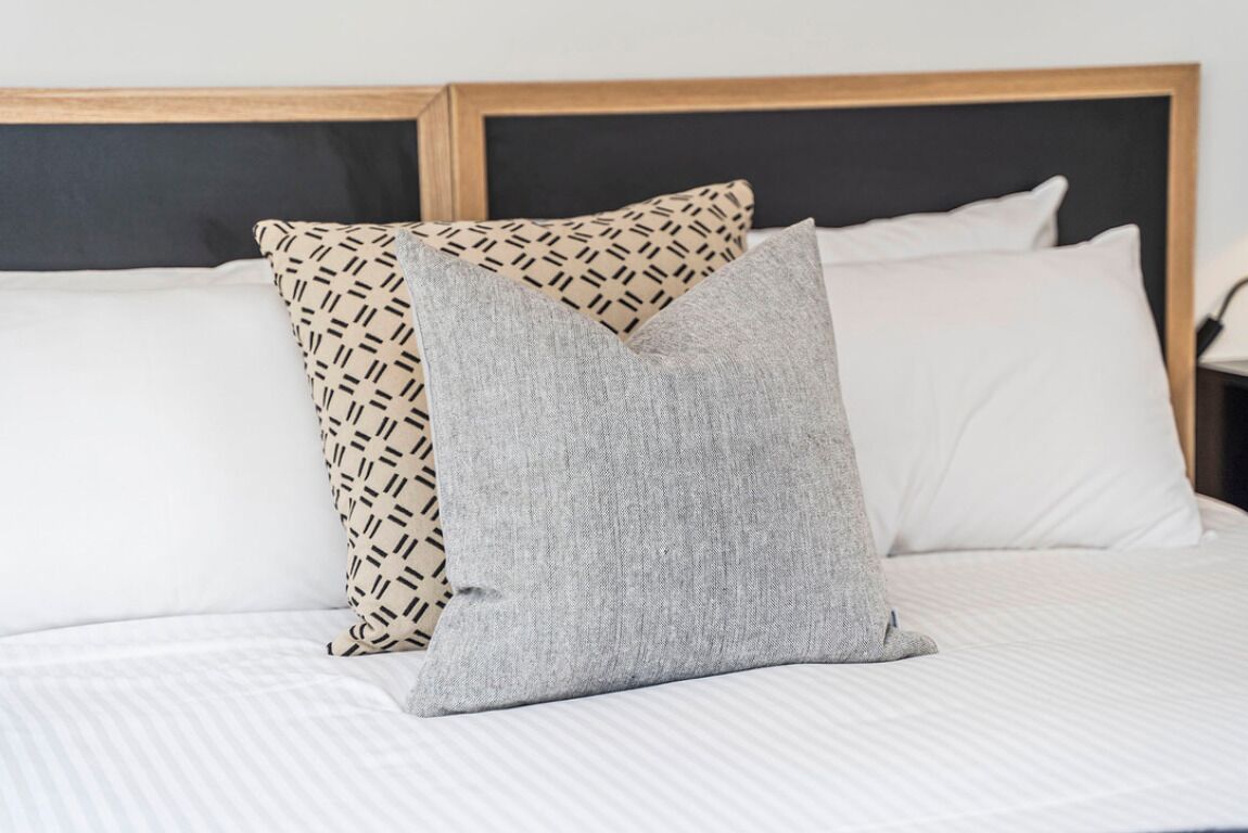 A bed with two pillows, one patterned and one solid grey, in a room with a wooden headboard.