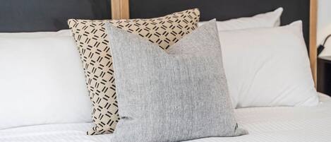 A bed with two pillows, one patterned and one solid grey, in a room with a wooden headboard.