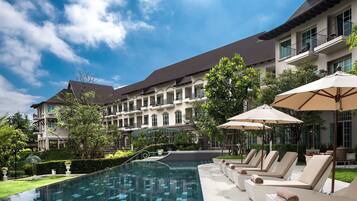 A hotel with a swimming pool, lounge chairs, and umbrellas.