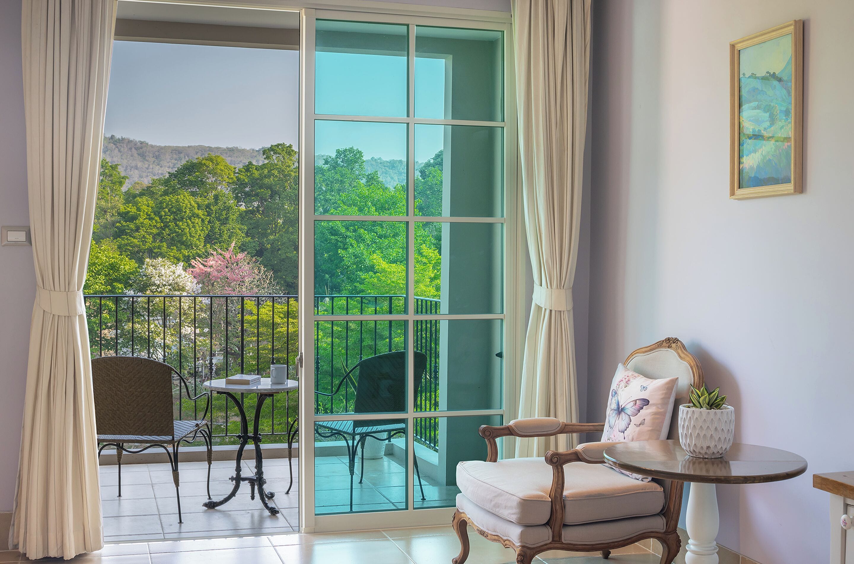 A balcony with a view of greenery and hills, a chair, a small table, and a potted plant.