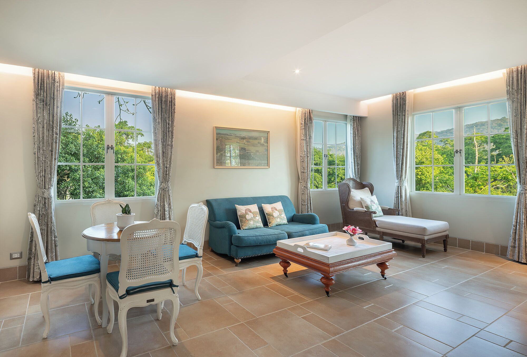 A spacious room with a blue sofa, a white chair, a wooden coffee table, and large windows with curtains.