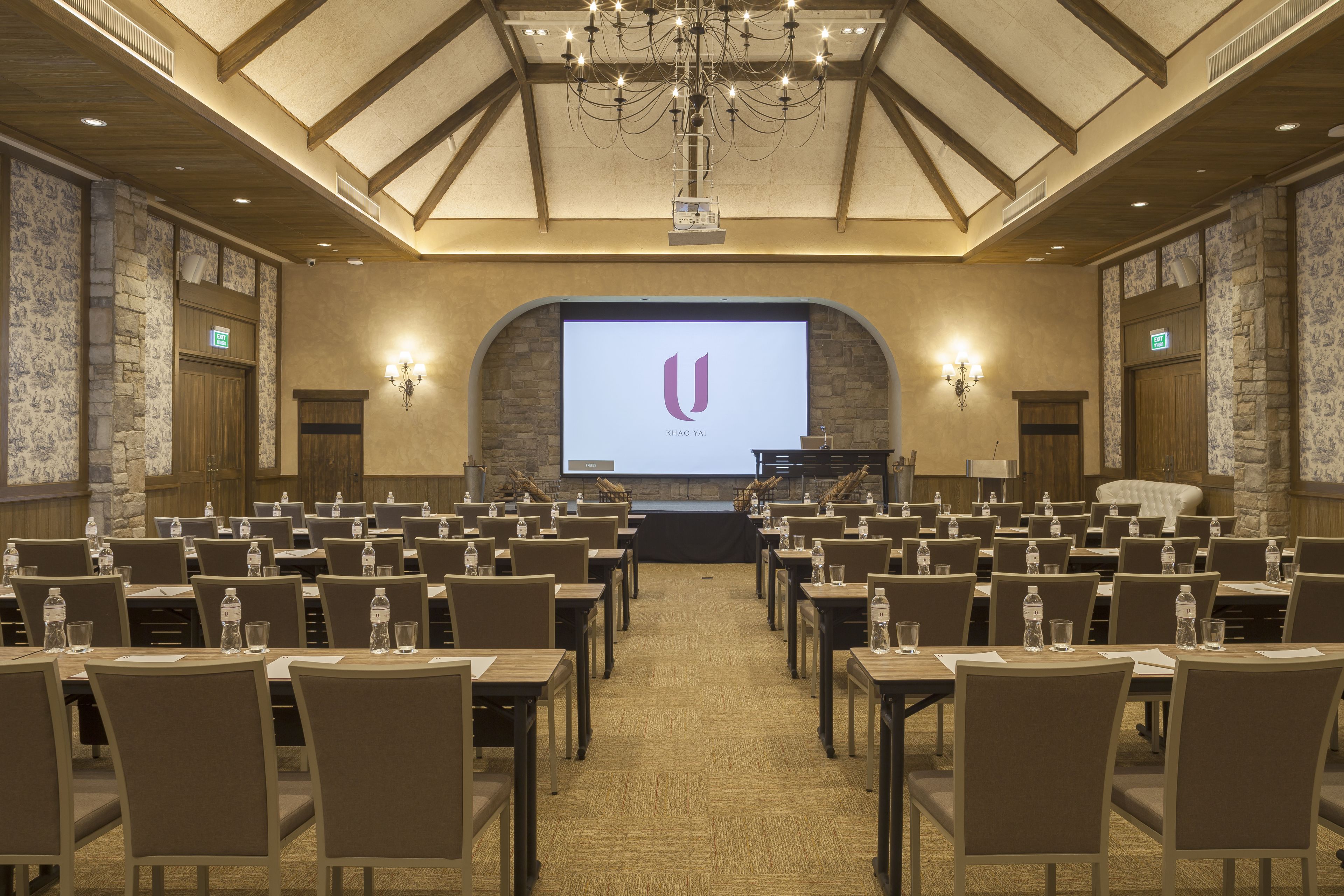A conference room with rows of tables and chairs, a projector screen, and a stage with a podium.