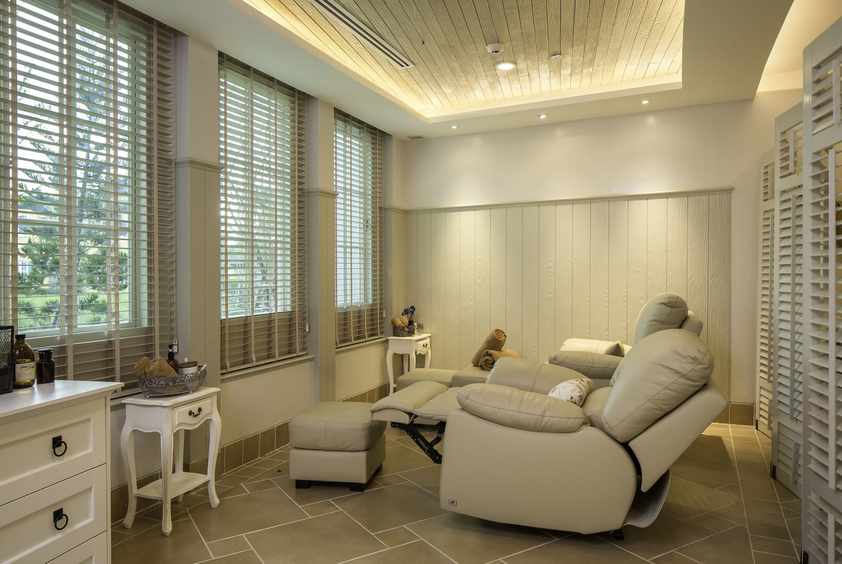 A spa room with a massage chair, a small table with a bowl, and a window with blinds.