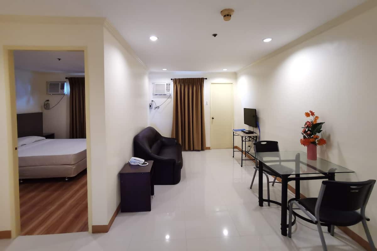 A hotel room with a bed, a desk, a chair, a telephone, and a small table with a vase of flowers.