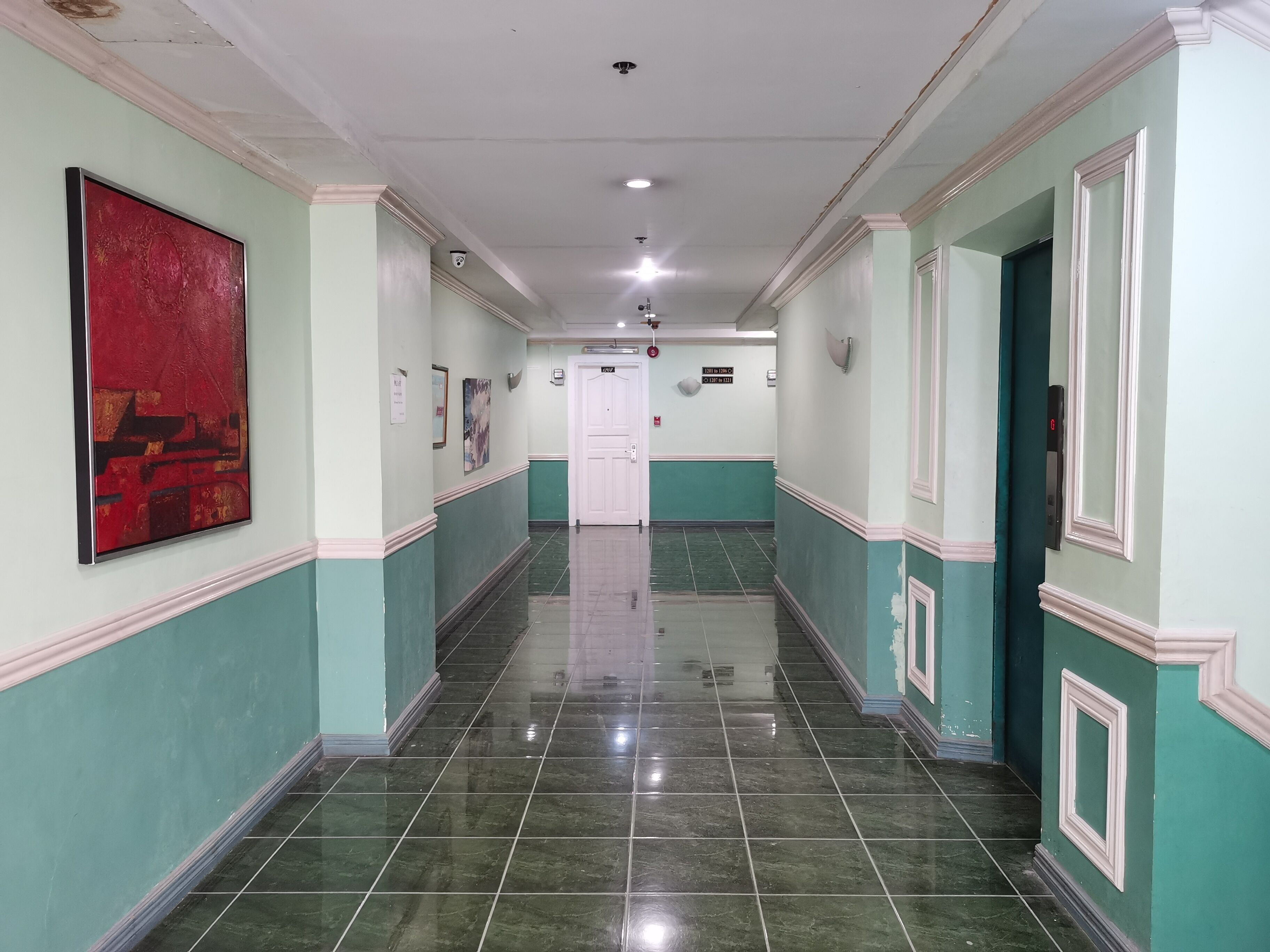 A hallway with green and white walls, a red abstract painting, and a white door at the end.