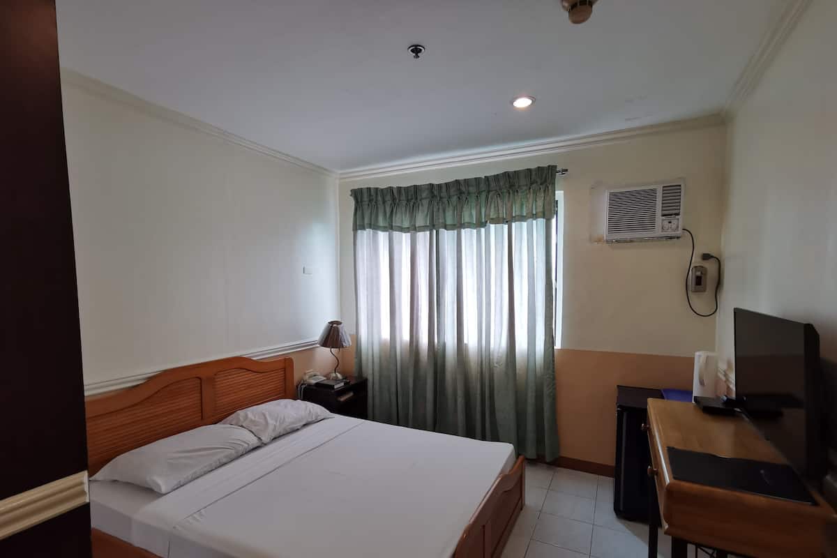A hotel room with a bed, a desk, a television, a lamp, and a window with curtains.
