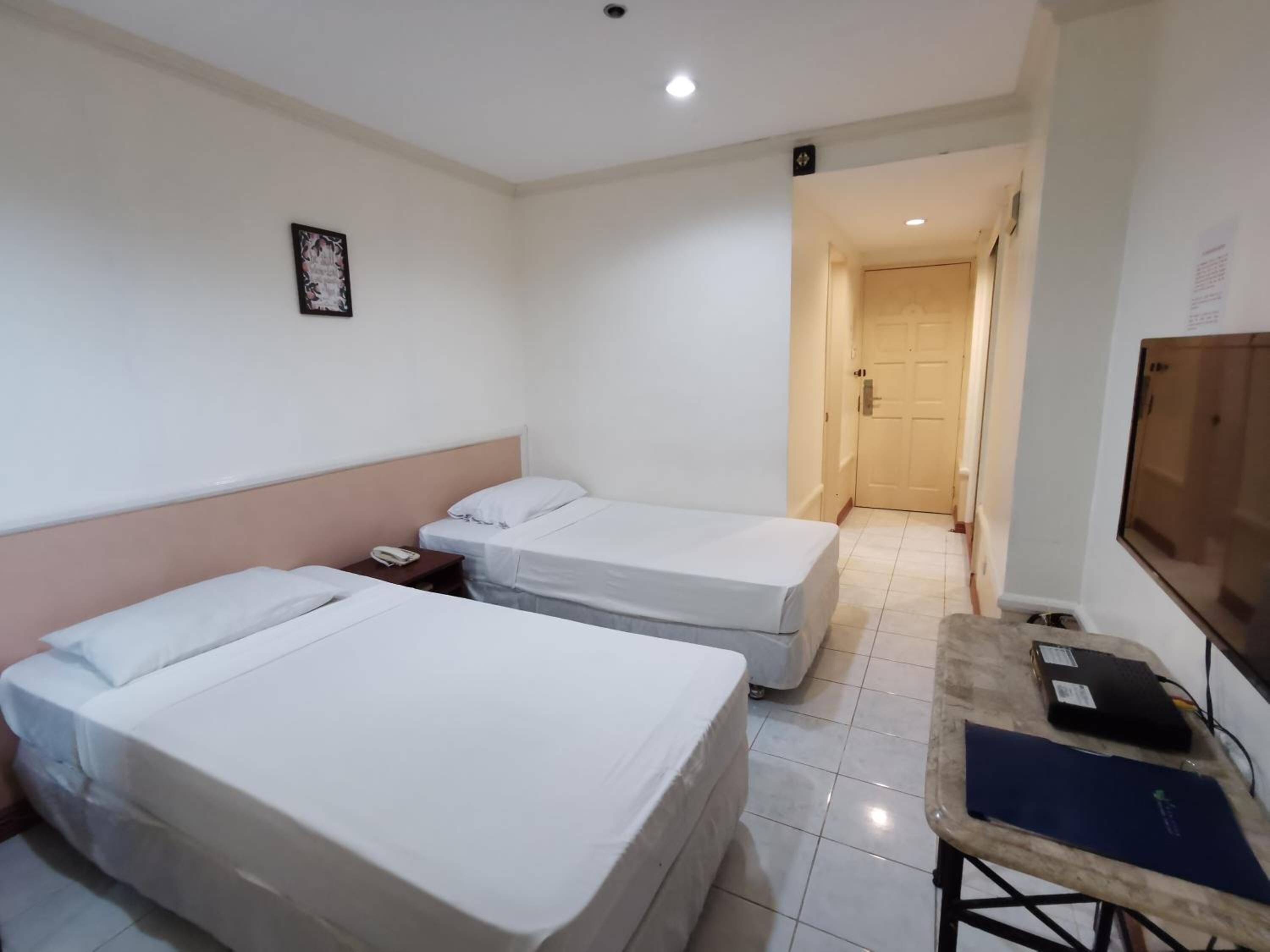 Ein Hotelzimmer mit zwei Einzelbetten, einem kleinen Tisch mit Telefon und Laptop sowie einem Fernseher an der Wand.