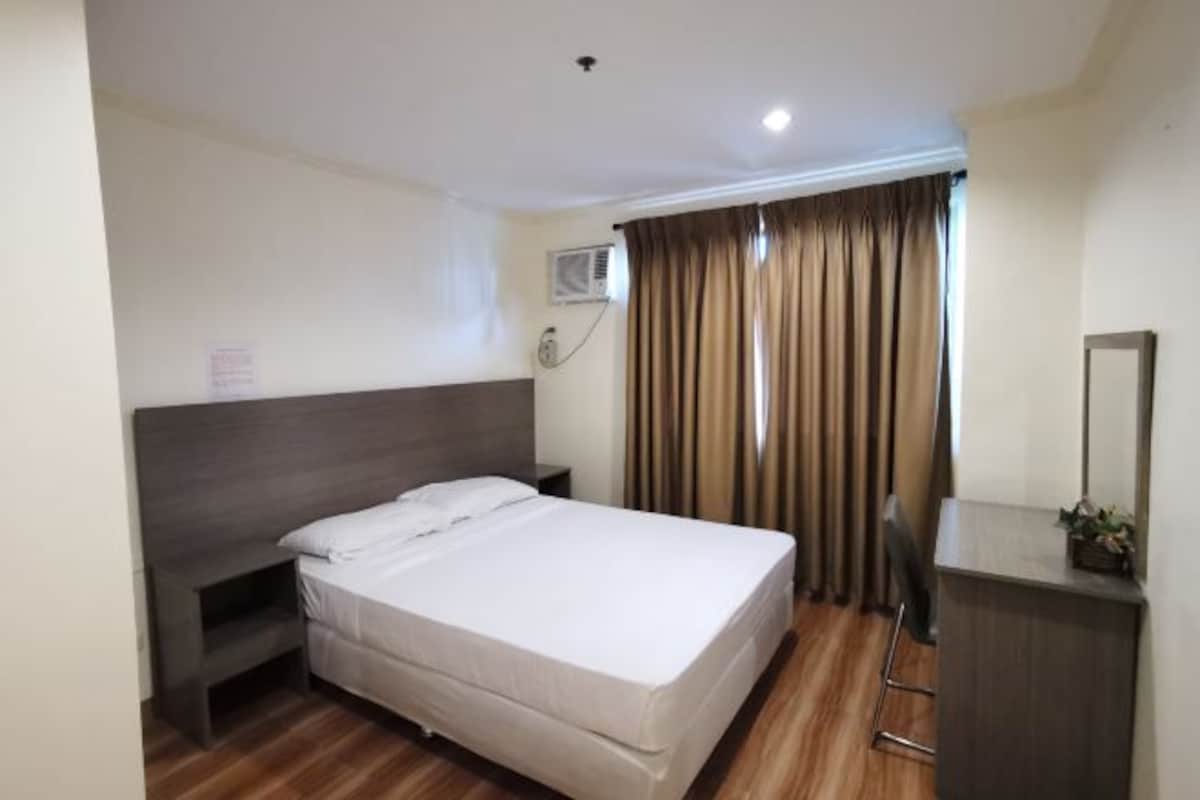 A hotel room with a bed, a nightstand, a desk, a mirror, and a window with curtains.