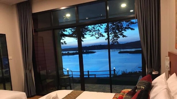 A hotel room with a large bed, a view of a body of water, and a balcony with curtains. - Khong Chiam Orchid Riverside Resort (Khong Chiam)