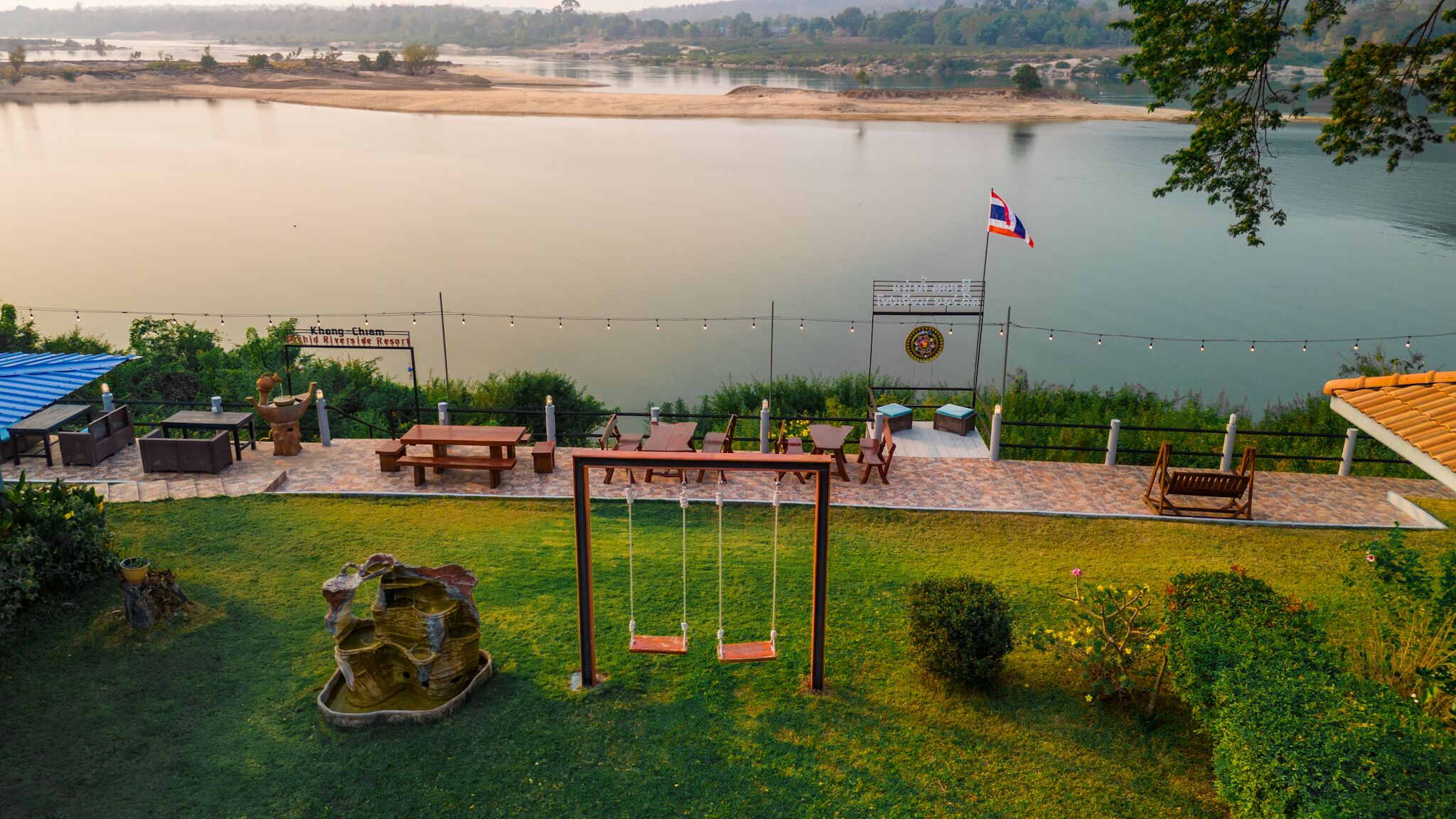 Un patio junto al lago con mesas de picnic, un columpio y una bandera.