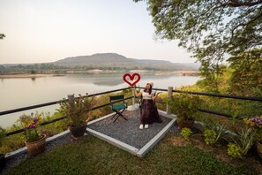 A woman standing on a balcony with a heart-shaped decoration, overlooking a lake with hills in the background. - Khong Chiam Orchid Riverside Resort (Khong Chiam)