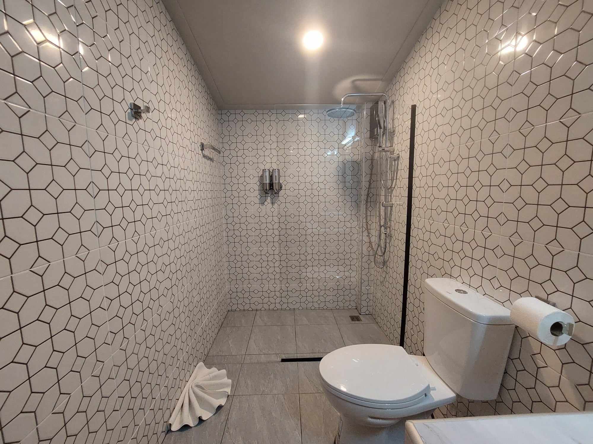 A bathroom with hexagonal patterned tiles, a toilet, a shower enclosure, and a towel on the floor.