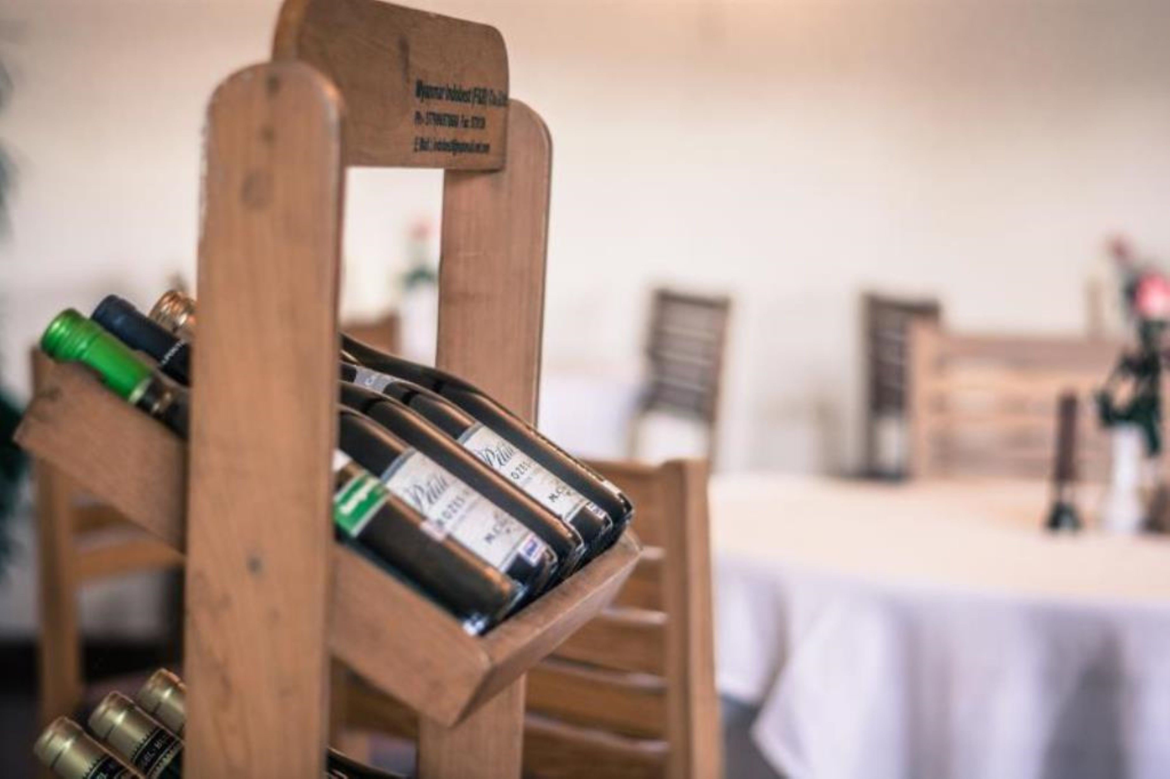 A wooden wine rack with bottles, a table with a white tablecloth, and a blurred background with a chair and a person.