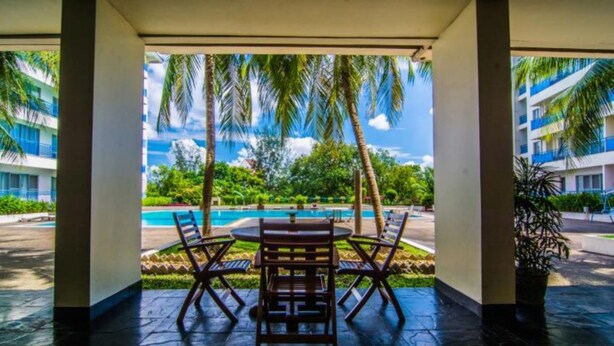 A covered outdoor seating area with a view of a pool and palm trees. - Sakura Residence (Yangon)