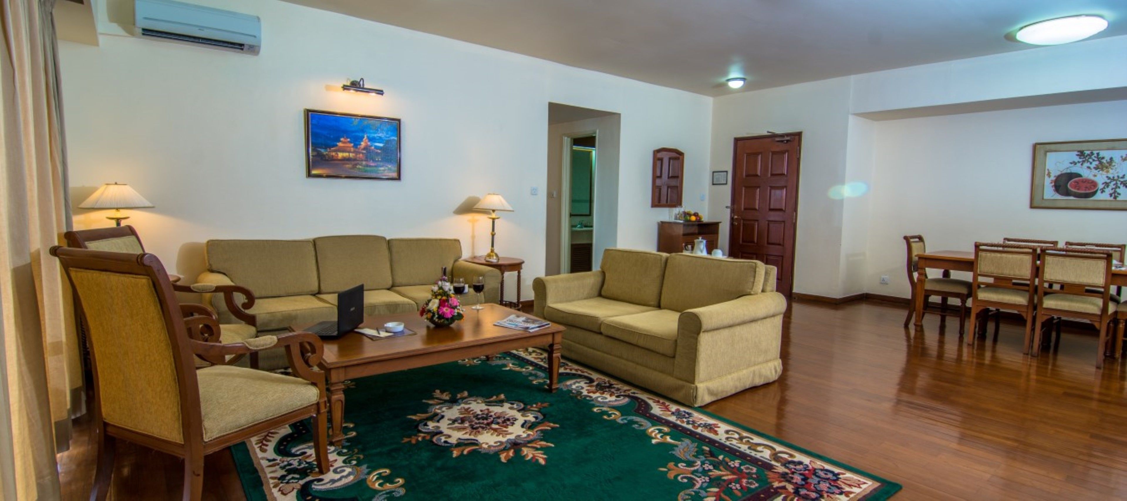 A living room with two sofas, a coffee table, a dining table with chairs, a lamp, and a painting on the wall.