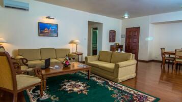 A living room with two sofas, a coffee table, a dining table with chairs, a lamp, and a painting on the wall.