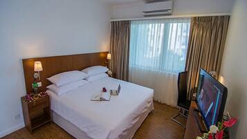 Una habitación de hotel con una cama, una mesita de noche, aire acondicionado, un televisor y una ventana con cortinas.
