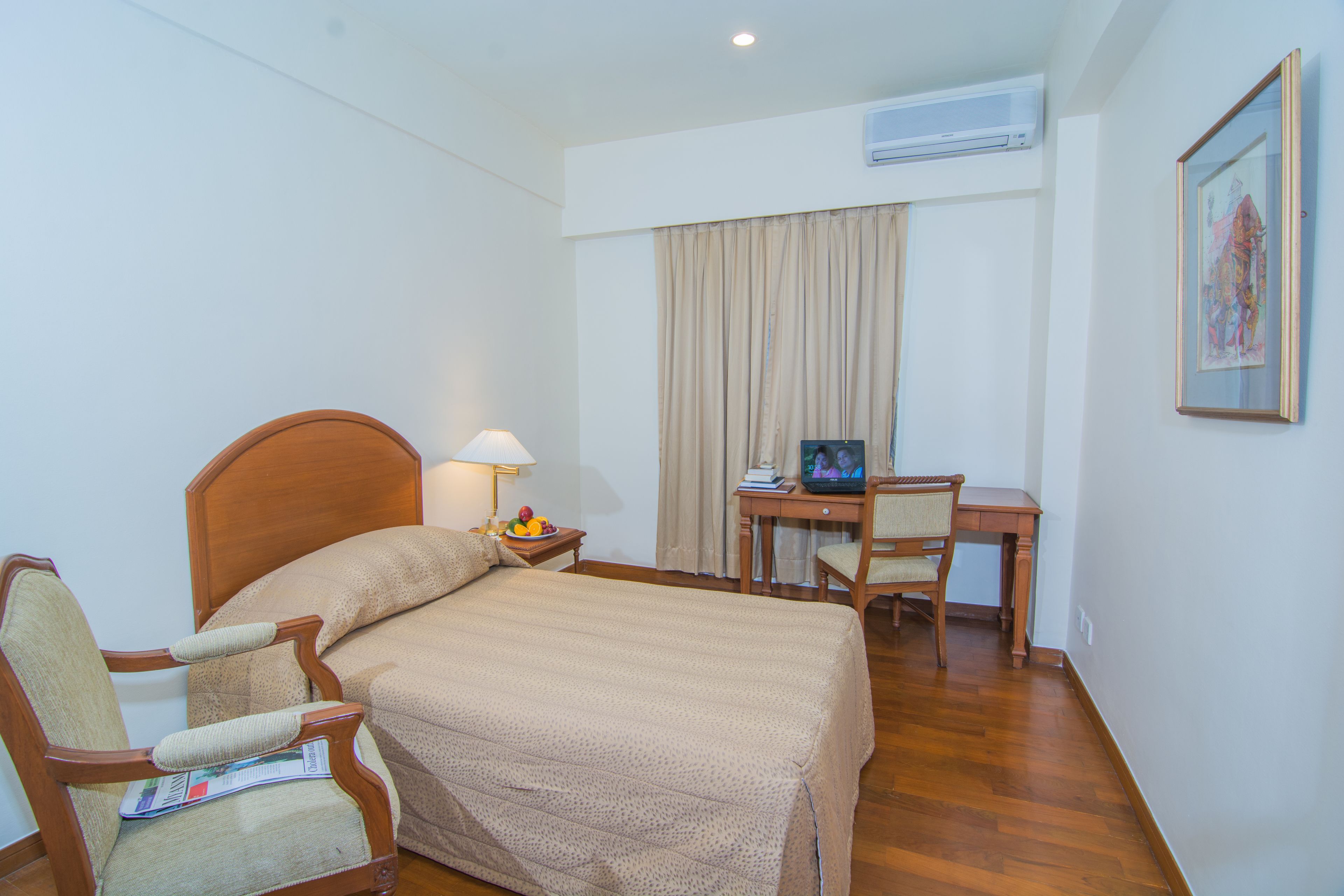 A hotel room with a bed, a desk, a chair, a lamp, and a television.