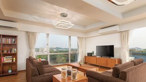 A modern living room with brown sofas, a wooden coffee table, a TV, and a bookshelf. - Sakura Residence (Yangon)
