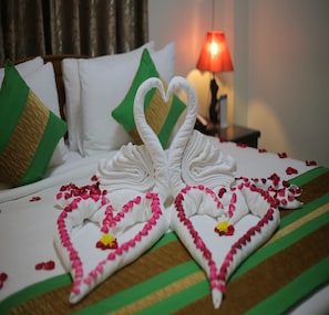 A bed with a heart-shaped towel arrangement and rose petals, green and white pillows, and a red lamp in the background. - Great Feel Hotel (Yangon)