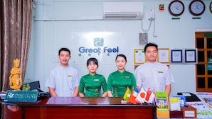 A hotel reception desk with a sign reading "Great Feel Hotel". There are four staff members standing behind the desk, and various flags and informational brochures are displayed on the counter. - Great Feel Hotel (Yangon)