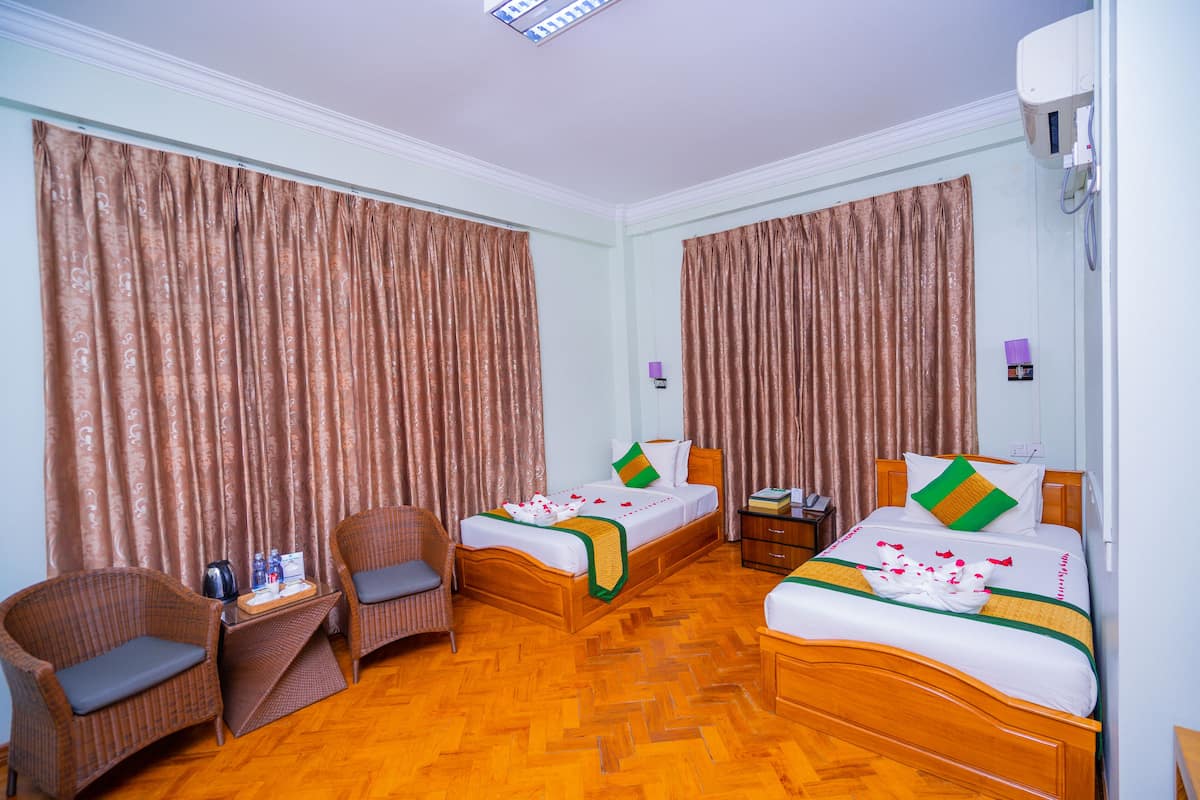 A hotel room with two beds, a sitting area with chairs, a small table with a kettle, and a nightstand.