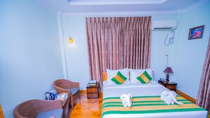 A hotel room with a bed, a chair, a nightstand, an air conditioner, and a wall-mounted phone. - Great Feel Hotel (Yangon)