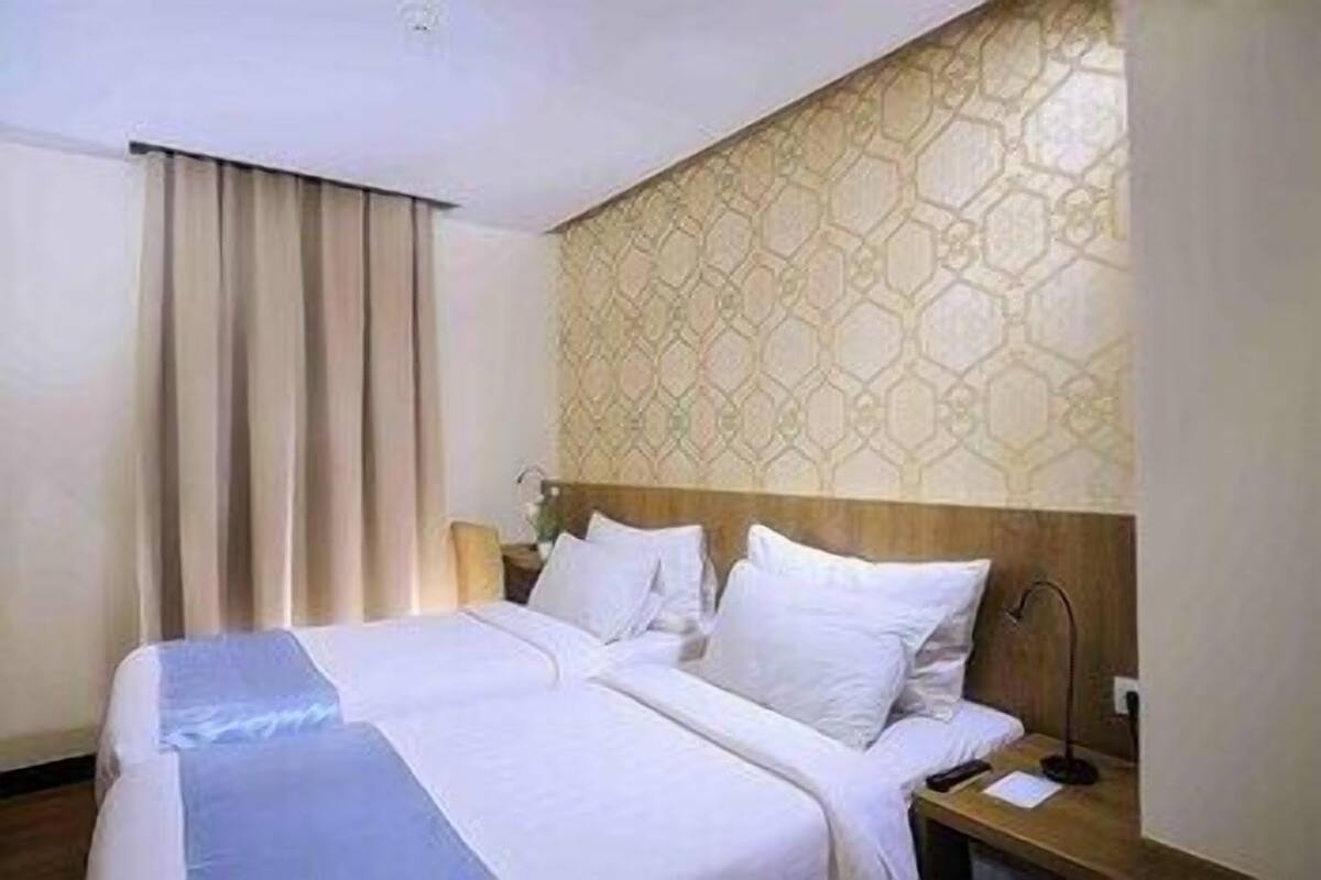 A hotel room with a large bed, a wooden headboard, a nightstand, and a patterned wall.