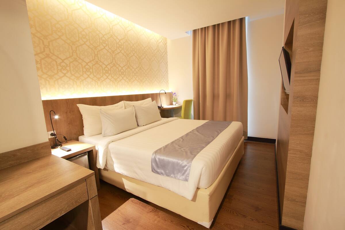 A hotel room with a large bed, bedside tables, a desk, a lamp, and a wall-mounted TV.