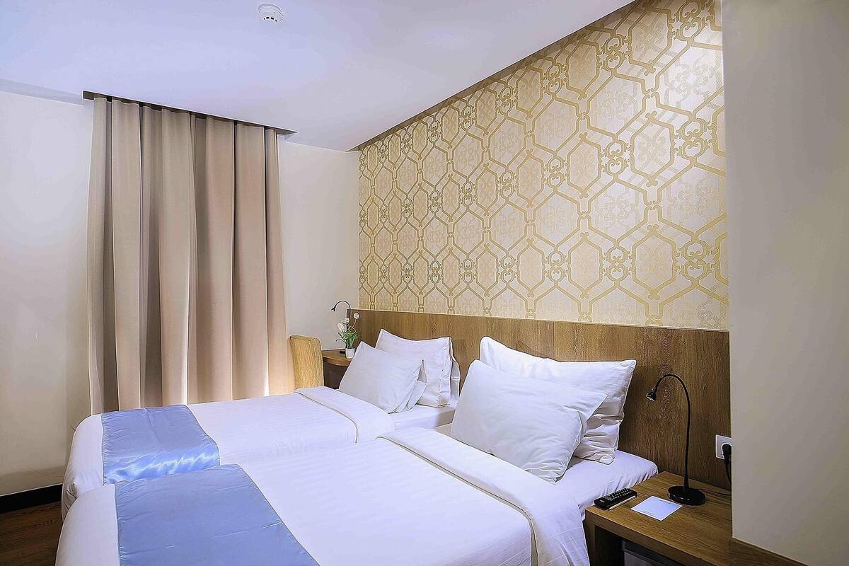 A hotel room with a large bed, a wooden headboard, a nightstand with a lamp, and a patterned wallpaper.