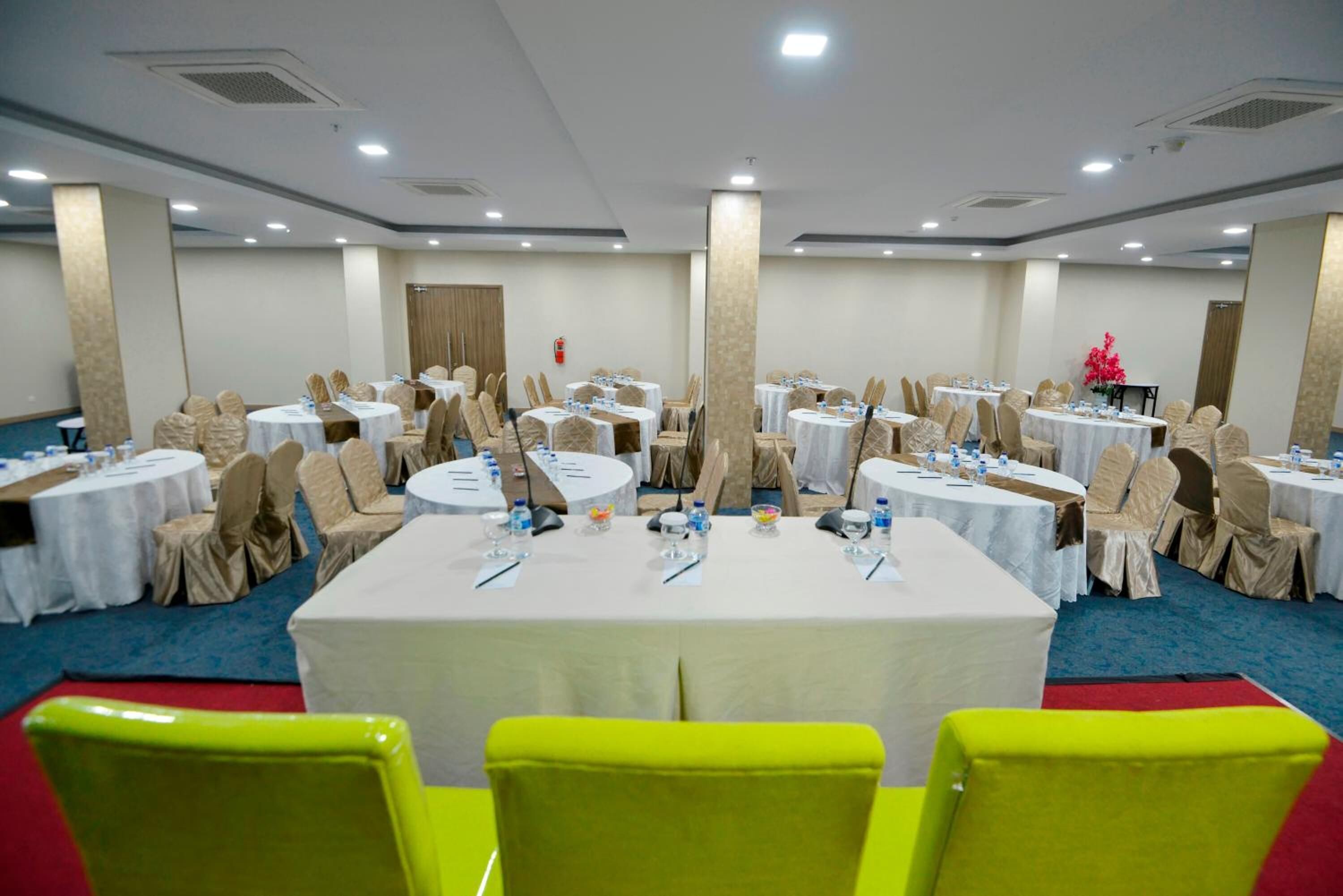 Un salón de conferencias con mesas redondas, sillas color beige y manteles blancos.
