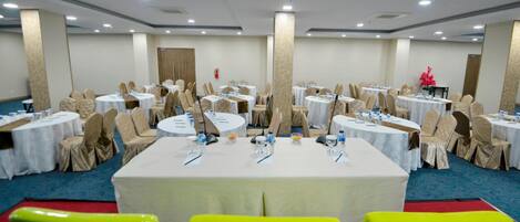 Un salón de conferencias con mesas redondas, sillas color beige y manteles blancos.