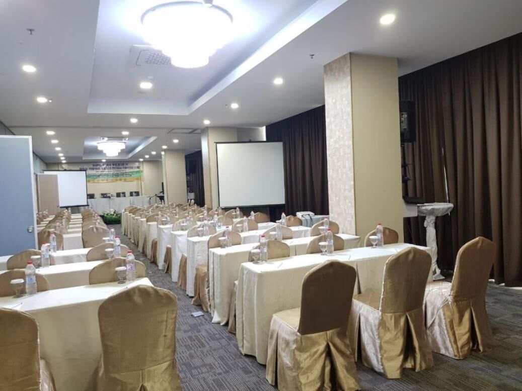 Une salle de conférence avec des rangées de tables et de chaises, un écran de projection et un pupitre.