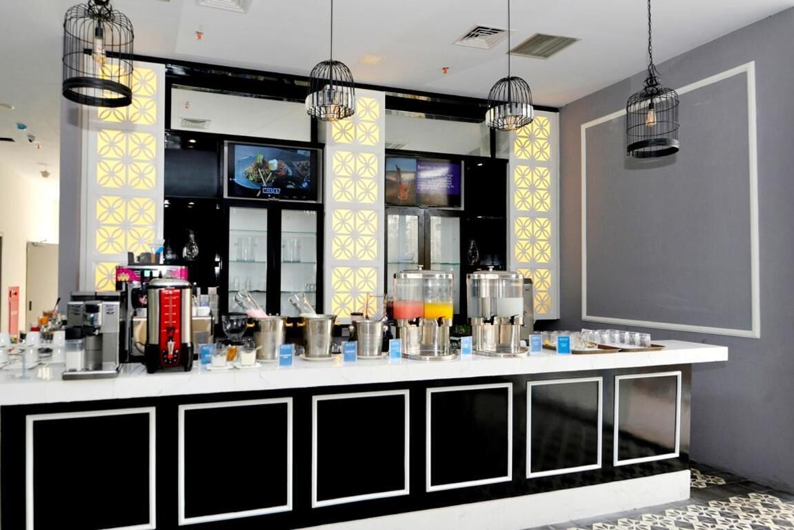 A modern bar area with a white countertop, black and white geometric wall panels, and multiple beverage dispensers.