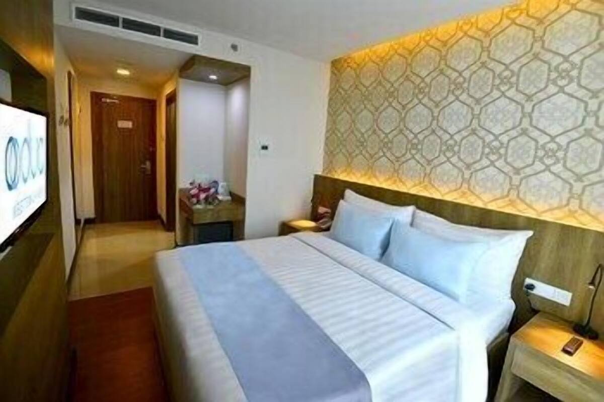 A hotel room with a large bed, a wooden headboard, a nightstand, a bedside table, and a wall-mounted TV.