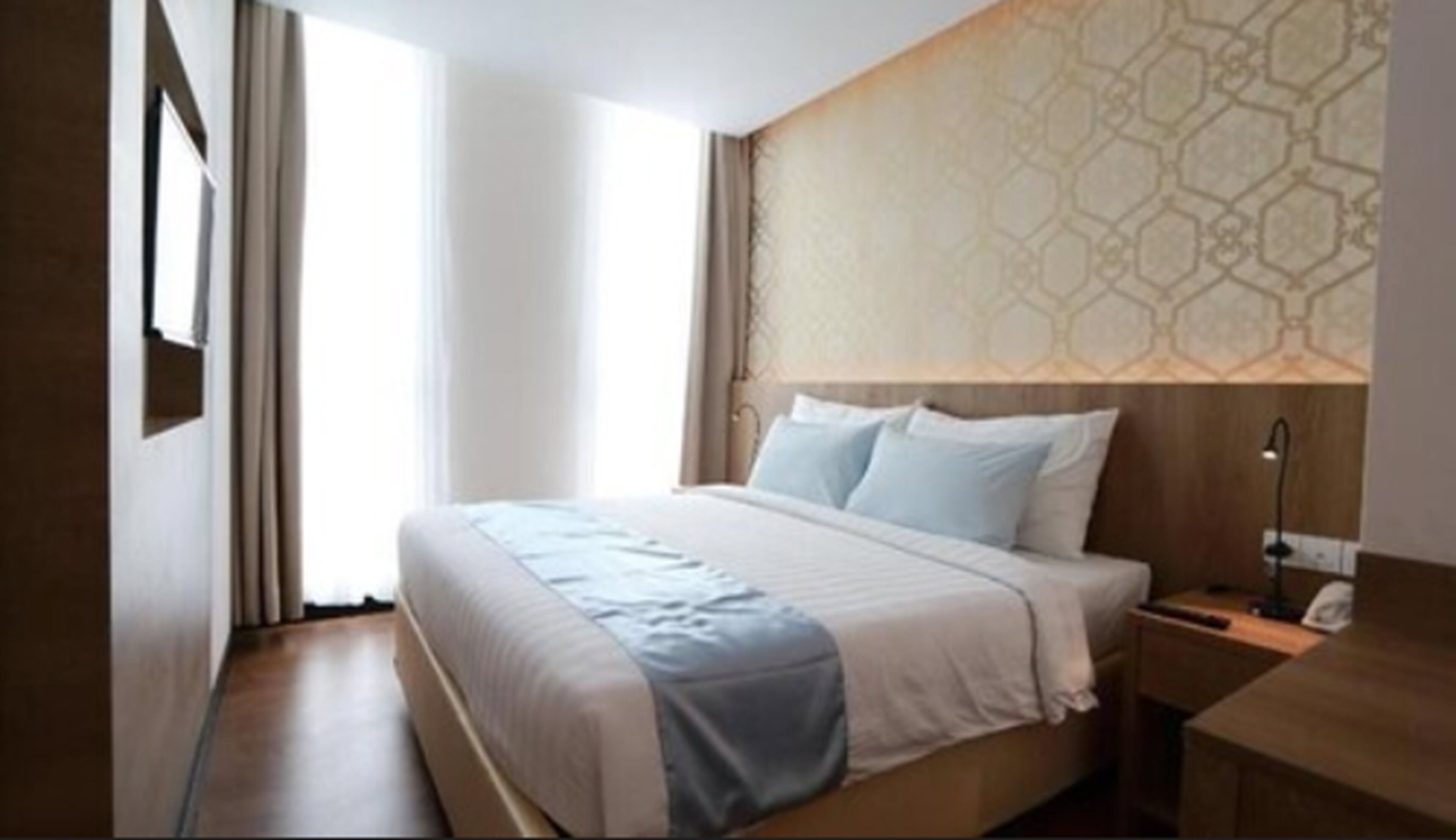 A hotel room with a large bed, a nightstand, a desk, and a patterned wall.